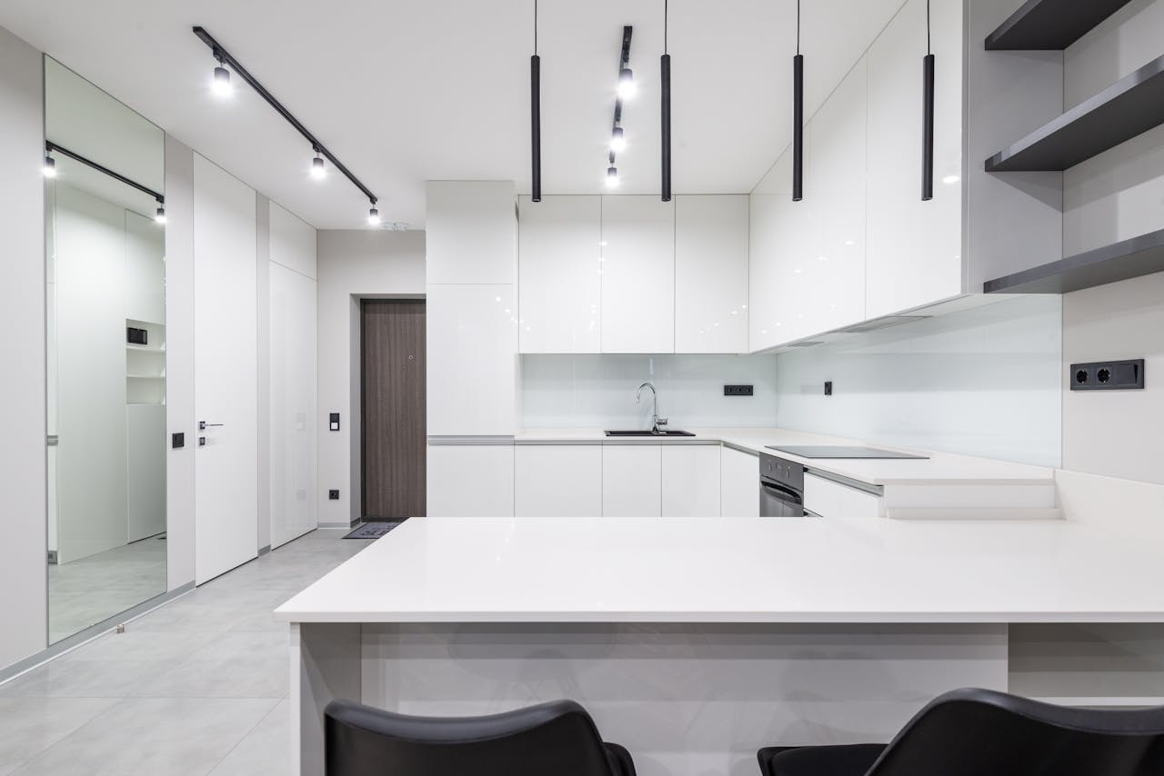 Services Elegant minimalist kitchen interior with white cabinets and modern lighting.